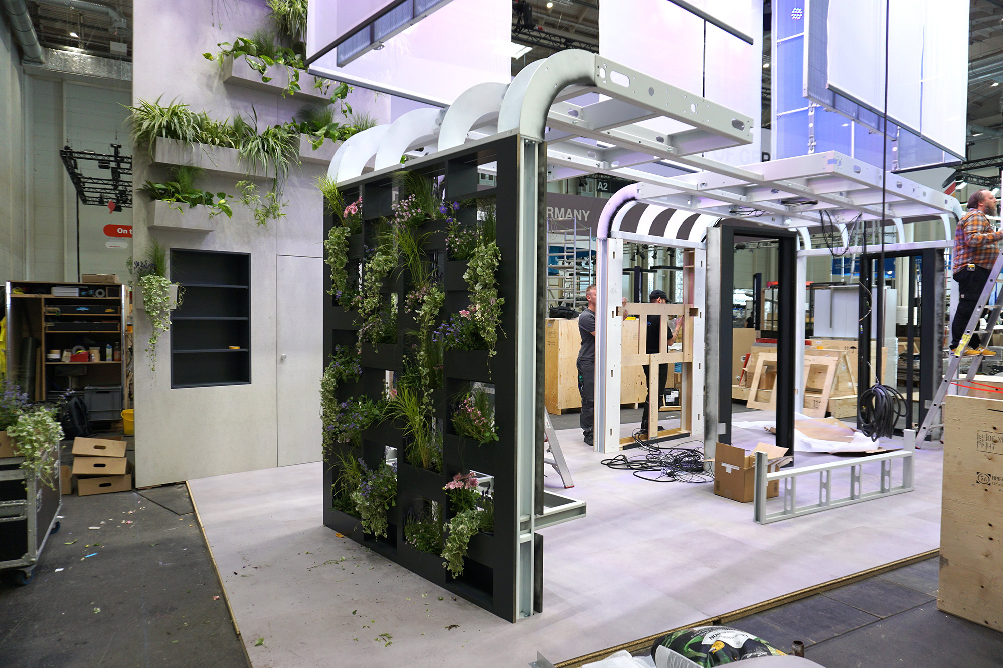 Modular Pavilion Assembly with Green Wall – “The Next Stop” by Luxoom Construction in progress of Luxoom’s future mobility pavilion, featuring modular frames and a vertical garden wall with live plants, at a trade fair booth.