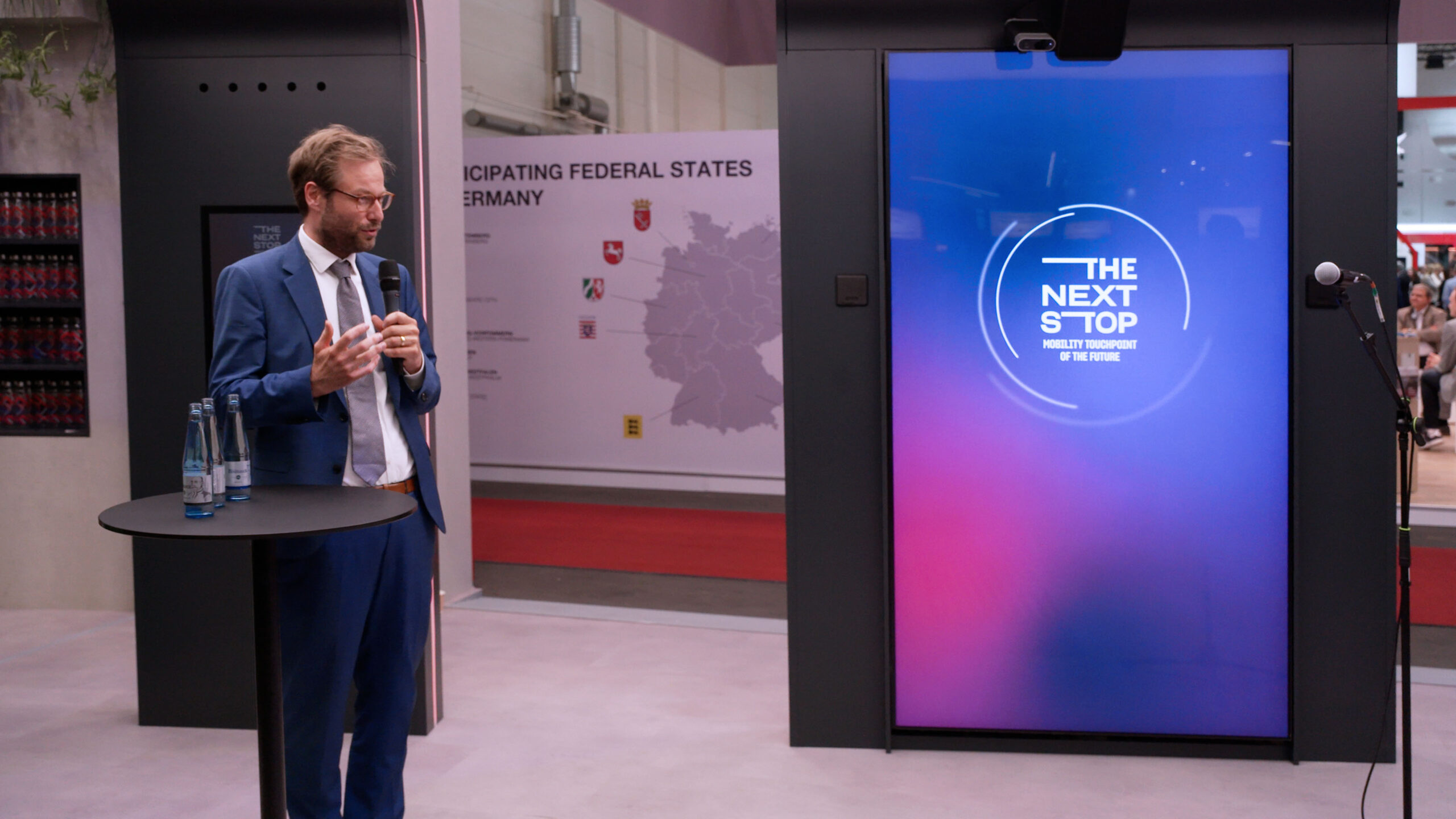 Anjes Tjarks at Press Conference at HVV’s “The Next Stop” – UITP 2025 Speaker presenting at HVV’s “The Next Stop” booth during a press conference at UITP 2025, with branding screen in the background.